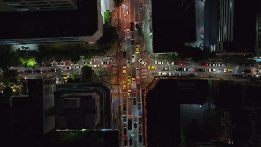 Top-down drone footage showing heavy night traffic at a busy intersection in Bangkok, Thailand. Cinematic pull-away shot with vibrant city lights.