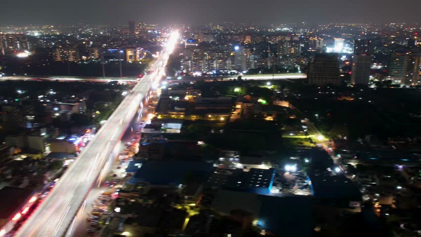 Aerial drone hyperlapse shot of Mumbai Delhi expressway showing fast moving cars in the middle of cityscape at night with skyscrapers in distance