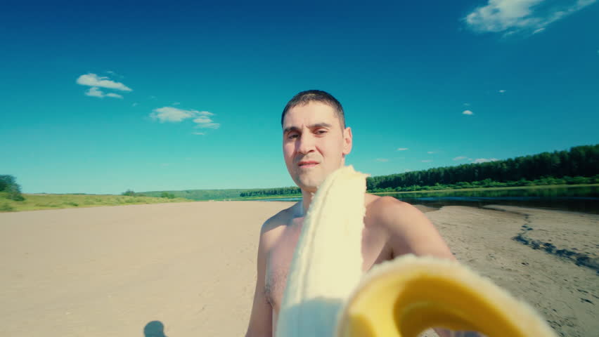 A guy is greedily eating a banana while relaxing on the beach. A man eating a fruit. A healthy lifestyle.