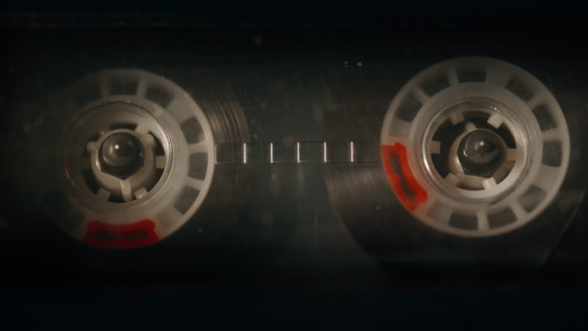 Audio cassette with spinning reels loaded in vintage deck closeup. Macro view classic magnetic tape rotating playing retro music indoors. Oldschool analog sound device performing melody. Old style.