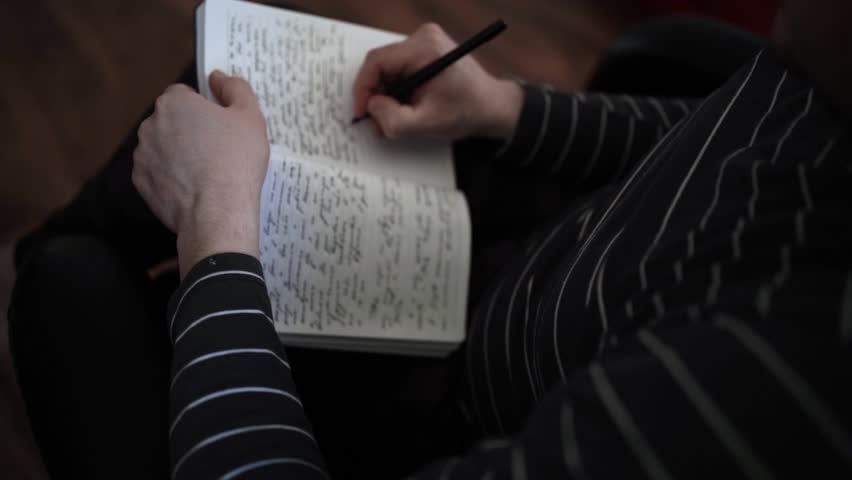 Close-Up of Person Writing in Notebook Wearing Striped Shirt, Seated