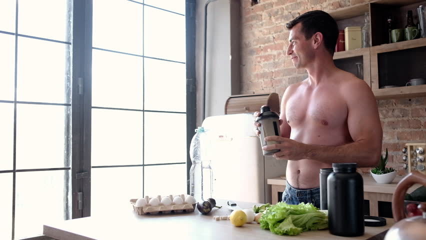 Young Athlete Man Preparing A Protein Shake In The Kitchen While Organizing Food And Sports Supplements For The Entire Day