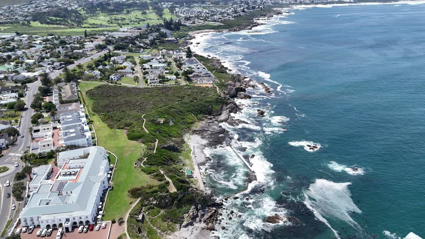 4K drone footage of coastal cliffs and ocean waves crashing against rocks in Hermanus, near Cape Town, South Africa. Scenic shoreline with mountain backdrop along the South Atlantic coast.