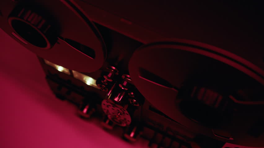 Vintage recorder spinning reels in dark room with red neon light closeup. Retro reel-to-reel device rotating recording sound indoors. Classic tape player working at playback session. Old technology.