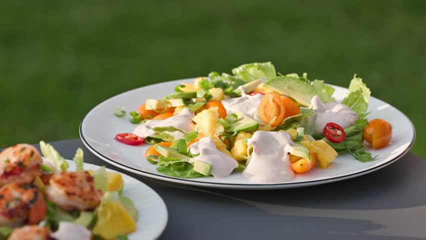 Chef put grilled shrimps on portion of freshly prepared healthy vegetable salad  on plate. outdoor cooking, food close-up