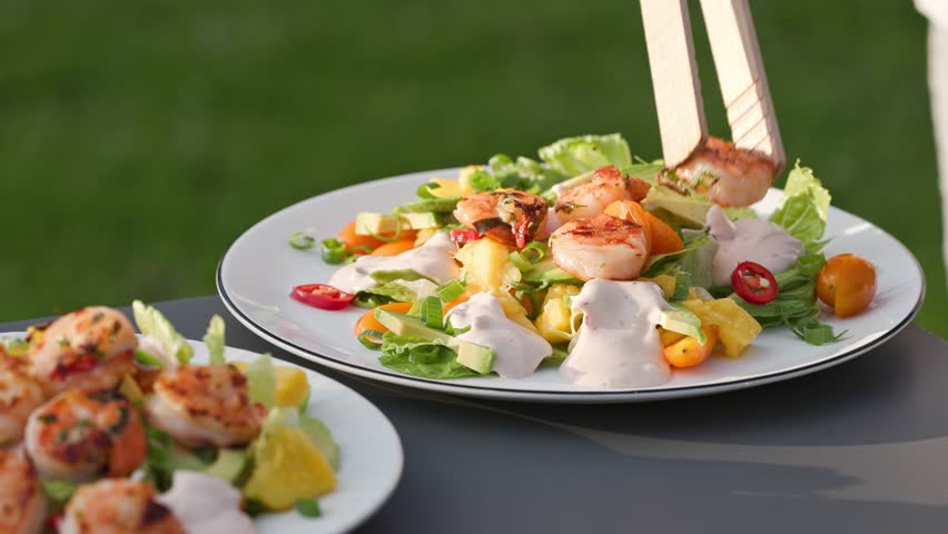 Chef put grilled shrimps on portion of freshly prepared healthy vegetable salad  on plate. outdoor cooking, food close-up