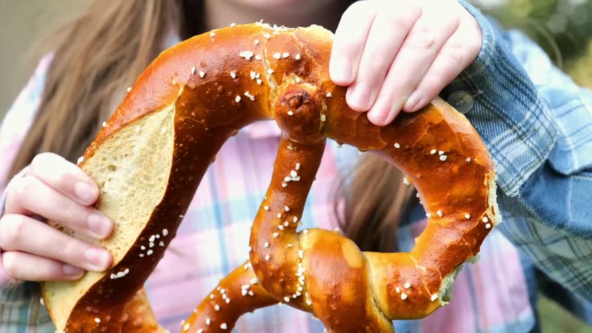 Pretzel in a girls hands. childs hand breaks off a fresh, crispy pretzel.Oktoberfest food traditional.