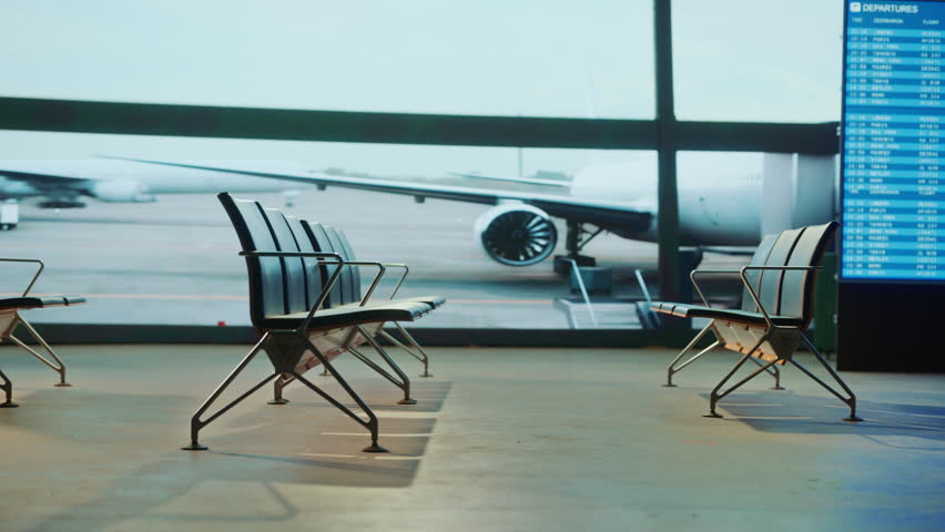 Empty airport seats stand in front of a large window, offering a view of airplanes on the tarmac