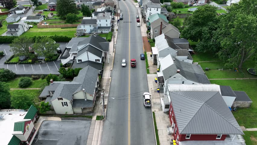 Driving cars in Main Street of small Americans town in summer. Green trees and garden grass of homes in historic city of Pennsylvania. Aerial backwards top down.