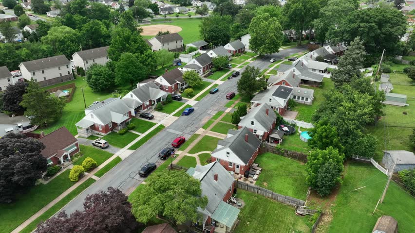Single family houses with red brick facade in suburb district of town. Green grass in garden. Quiet atmosphere. Aerial flyover shot. Middle class housing area of USA.