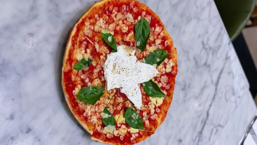 Overhead view of fresh Italian pizza with basil leaves, ricotta, and parmesan on a marble surface. Ideal for food, ads, or restaurant content.