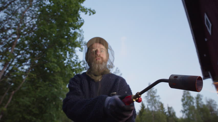 Eccentric man with crazy eyes wearing mosquito head net waves around blowtorch