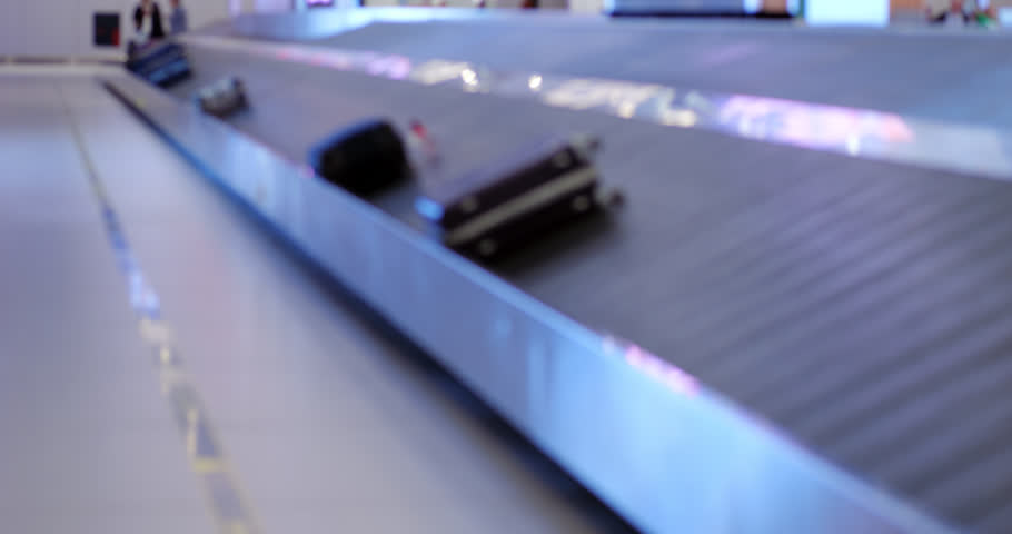 Unclaimed suitcases on move on luggage carousel, slow motion blurred view of arrivals hall at modern international airport. Concept of commonness of air travel nowadays