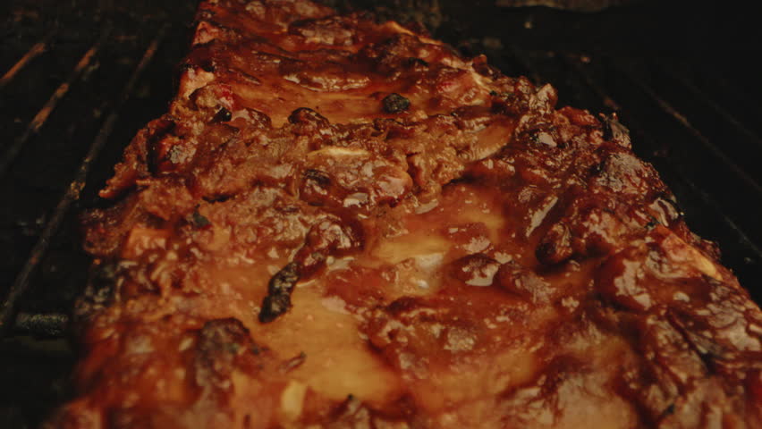 Beautiful macro dolly in of grilled ribs on a barbecue. The meat is juicy and nicely cooked