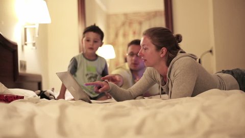Happy family with laptop lying on bed, steadicam shot
