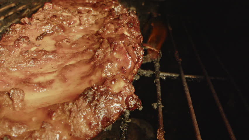 Close up of flames underneath a slab of spareribs being grilled on a barbecue