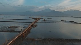 Aerial shot of a tranquil lake at dawn. Fishermen prepare traditional wooden boats by a bamboo bridge, with majestic mountains in the background. A serene, scenic view of rural life. - Powered by Shutterstock - Get 15% off with code: PIKWIZARD15
