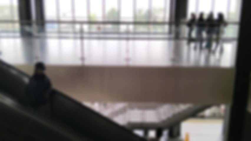 The atmosphere shows silhouettes and bokeh inside the train station building. People are passing by, some are going down the escalator, some are walking in the crowd. It was made with fast movement.
