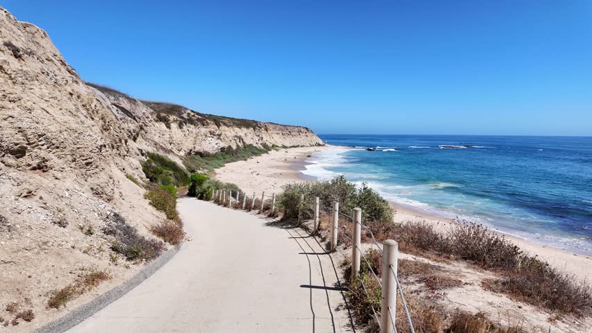 Newport Beach CA walking path that leads down to the beautiful beach with small waves coming from the Pacific Ocean blue sky and no clouds.
