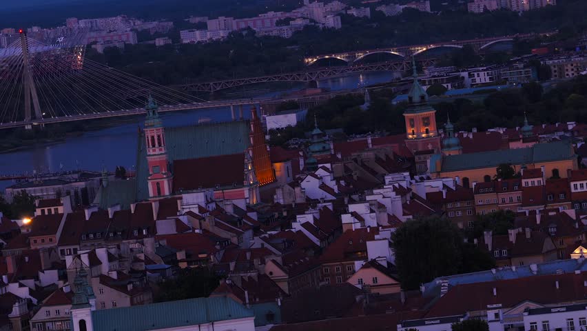 Bridges over Vistula River and old town with towers in Warsaw, Poland. Aerial wide rotating shot. Night scene with dark blue sky and lighting city.