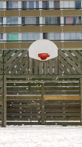 Snowy basketball hoop in social housing neighborhood, slow motion pull out shot evoking urban childhood
