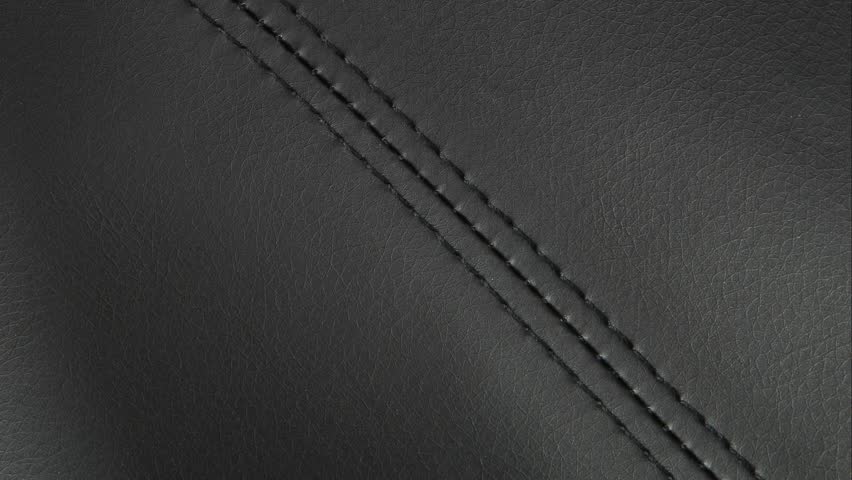 Camera tracks the seam, revealing grain and thread on premium leather