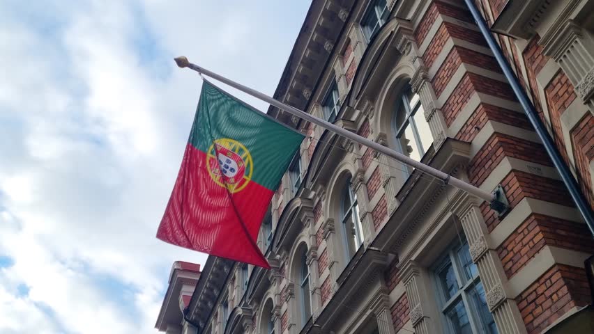 A Portuguese flag hangs outside the embassy building in Stockholm, Sweden, gently waving against a cloudy sky on a calm day