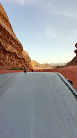 Rugged four-wheel drive vehicle traversing vibrant red sandy terrain amid the dramatic desert landscape of Wadi Rum, Jordan, capturing raw wilderness adventure
