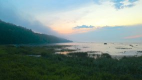 Stunning aerial drone footage gliding over grassy and reed filled beach area and continiues to fly over Baltic ocea sea during orange sunset, steep cliff bank in fog and mist visible on the left. - Powered by Shutterstock - Get 15% off with code: PIKWIZARD15