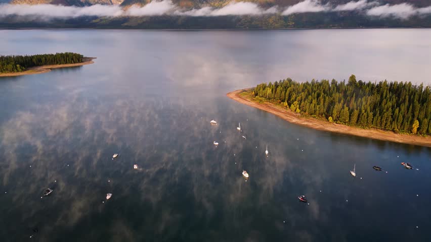 Aerial view of boats on Jackson Lake, with snow-capped mountains in the background under a cloudy sky, Teton County, United States.
