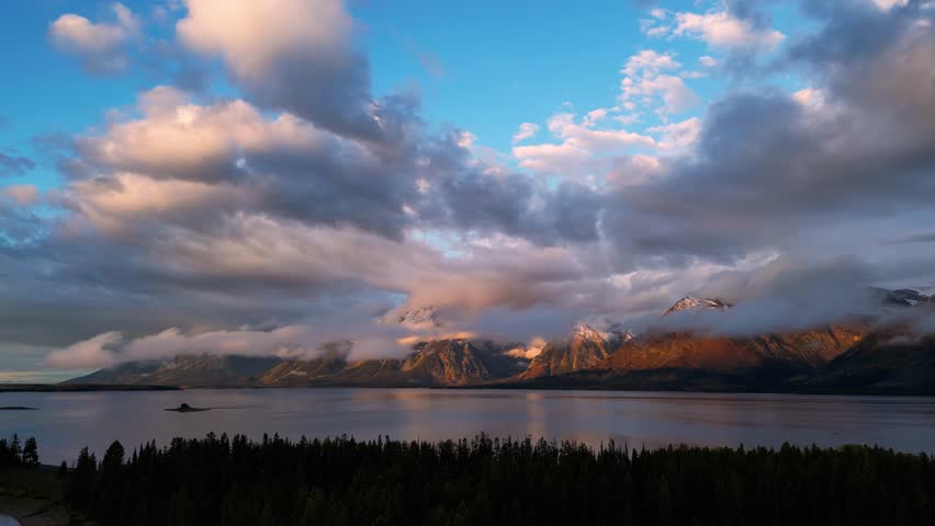 Aerial view of snow-capped mountains meet the still lake waters, under a sky filled with clouds, Grand Teton National Park, Teton County, United States.