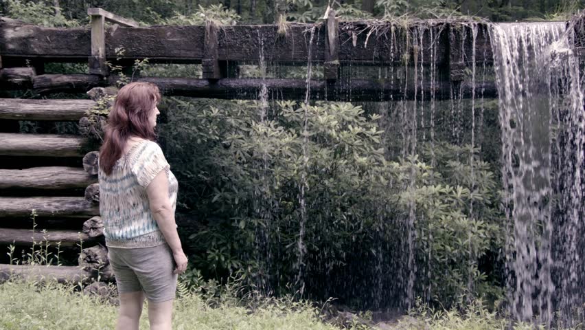 Middle aged woman with red hair walking near water falling from the Mingus Mill in the Great Smoky Mountains National Park in slow motion.