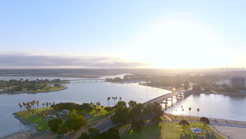 Aerial view of the bridges over glistening water, with palm trees lining the shores, and the sun creating a lens flare, San Diego, California, United States.
