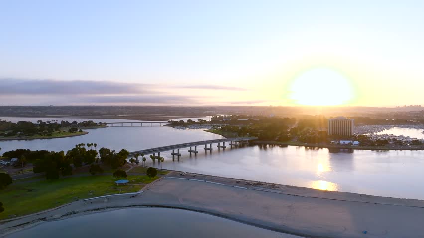 Aerial view of bridges stretching across tranquil waters, meeting sandy beaches under the bright sun, San Diego, California, United States.