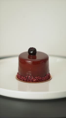 Slicing a glossy chocolate mousse cake topped with cherry. Elegant gourmet dessert on white plate, perfect for pastry, food, or restaurant visuals.