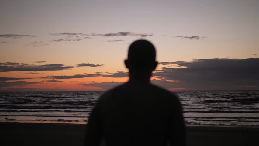Silhouette man walking toward calm sea at dawn in slow motion symbolizing reflection resilience and mental health