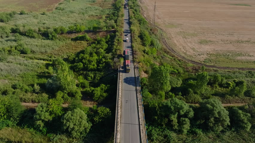 Specialized Heavy-Haul Trailer With Power Transformer Driving Along The Road Bridge Over The River. - aerial shot