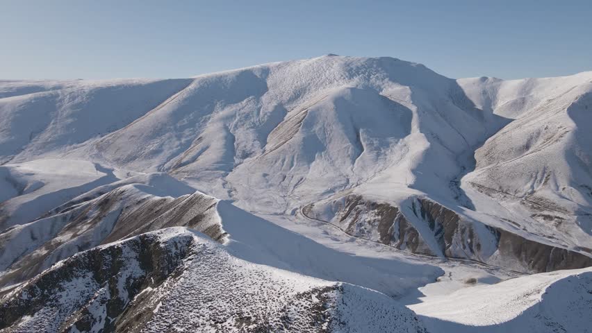 Curved aerial flight over a snow-covered ridgeline with sweeping views of surrounding alpine terrain in the Southern Alps near the Lindis Pass, New Zealand