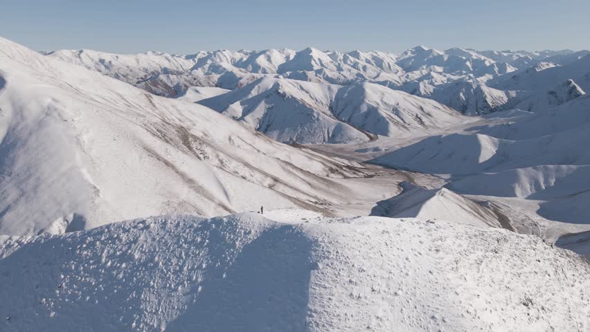 360-degree aerial orbit around a person standing on a snow-covered ridgeline surrounded by vast alpine peaks of the Southern Alps of New Zealand