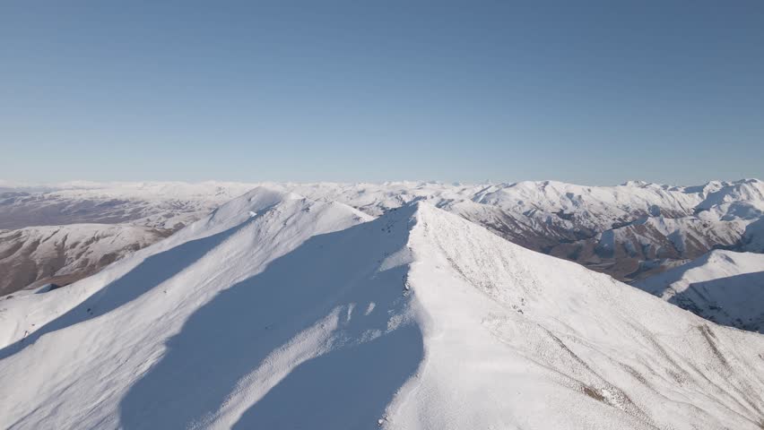 Wide angle aerial rising shot revealing an expansive snow-covered mountain range stretching across the Canterbury and Otago regions of New Zealand