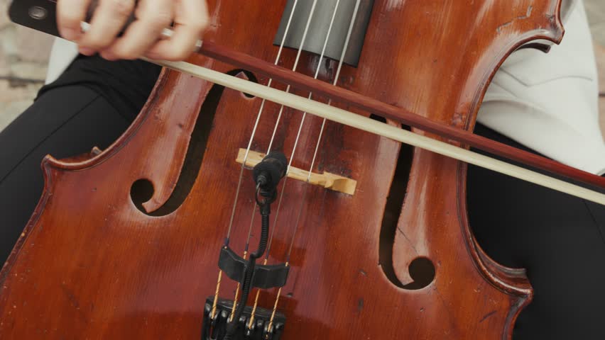 Close-up of musician playing cello with bow, detailed view of strings and wood instrument. Cello Performance at Wedding Ceremony