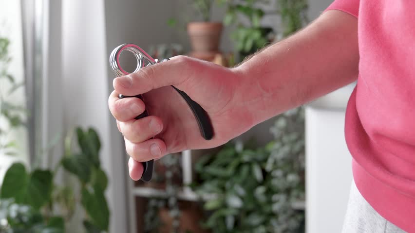 Man hand squeezing spring hand exerciser. Grip strength, arm lifting, muscle resistance, hand therapy and finger flexibility, rehabilitation tool, physical therapy aid, stress releasing practice