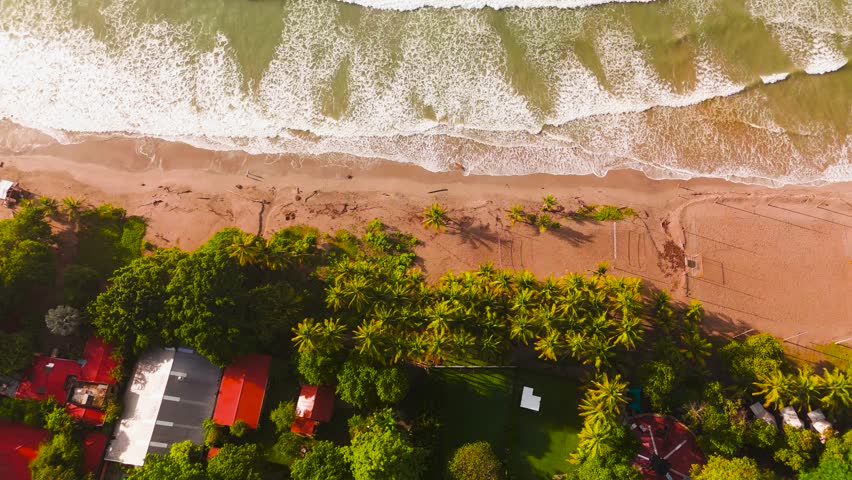 Drone video of a sandy beach in Costa Rica. The topdown shot shows waves crashing onto the shore, and a small town along the coast