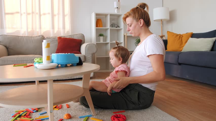Young mother singing song to daughter while sitting on the floor in the living room