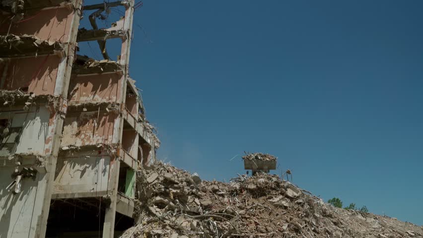 Industrial cleanup in progress with machinery pushing debris from a collapsed apartment building after demolition or structural failure.