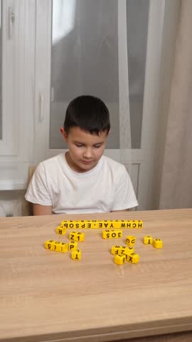 A boy makes words from cubes while sitting at a table.