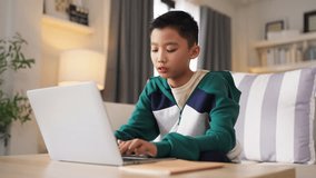 smart and cheerful Asian boy studies at home, typing on his computer and using a smartphone to access social media and e-learning platforms. With schools closed living room kitchen interior home - Powered by Shutterstock - Get 15% off with code: PIKWIZARD15