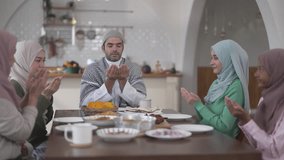 Muslim family praying before eating iftar meal during ramadan or eid together around dining table, tradition faith gratitude love, islamic culture peaceful moment with food and family, halal food - Powered by Shutterstock - Get 15% off with code: PIKWIZARD15