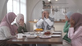 Muslim family praying before eating iftar meal during ramadan or eid together around dining table, tradition faith gratitude love, islamic culture peaceful moment with food and family, halal food - Powered by Shutterstock - Get 15% off with code: PIKWIZARD15