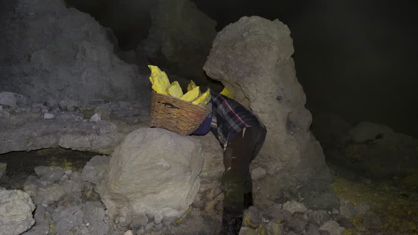 A sulfur miner working inside the volcano wearing a gas mask as protection for the toxic fumes.